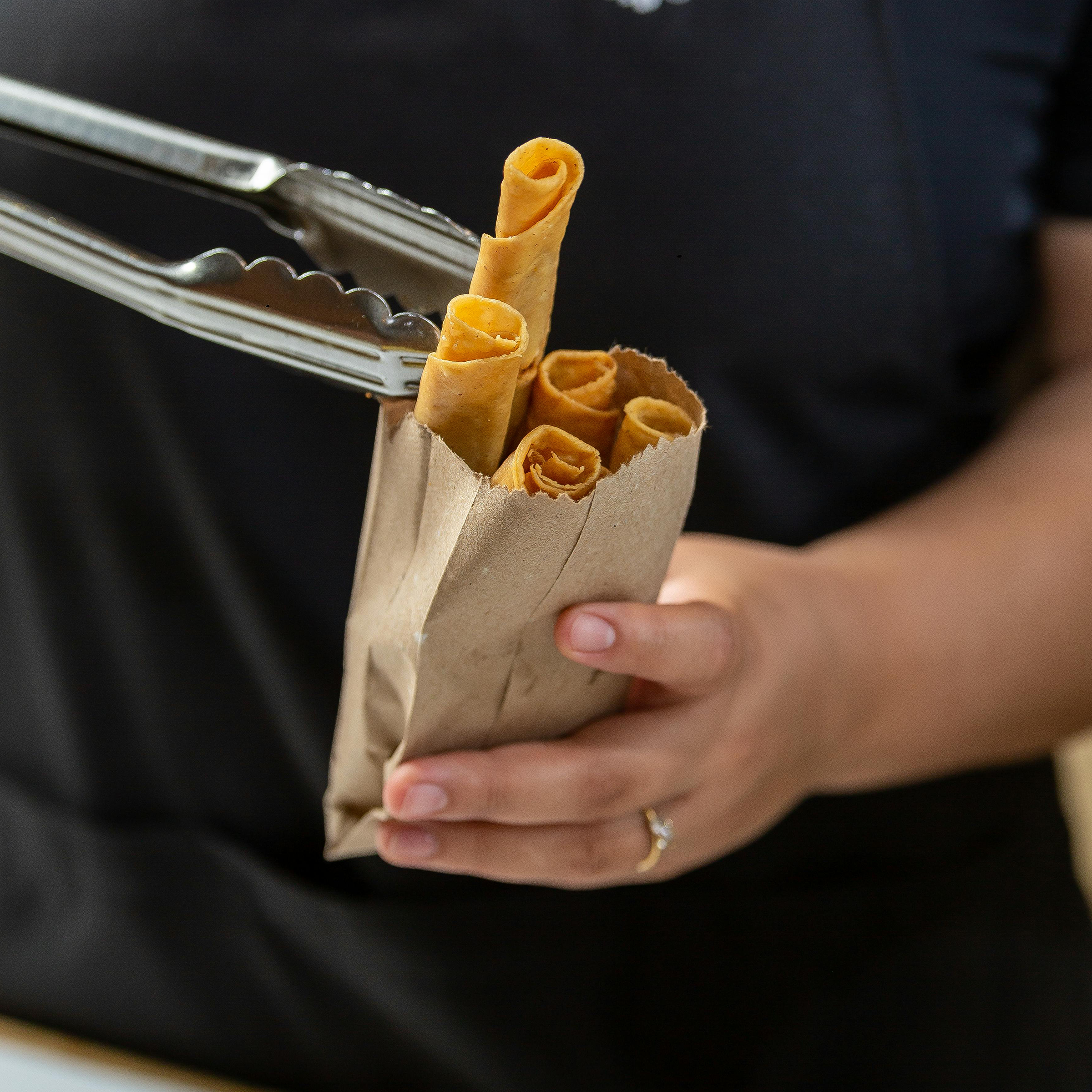 Hand holding and filling a baggie of crispy, tasty taquitos with tongs.