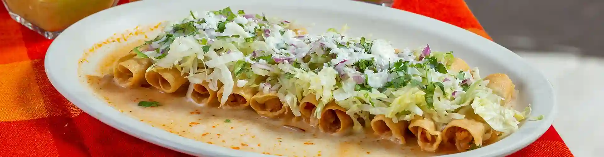 Plate of a row of taquitos dressed with delicious condiments and delectable garnishes.